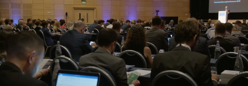 image shows several people listening to a speaker at a conference